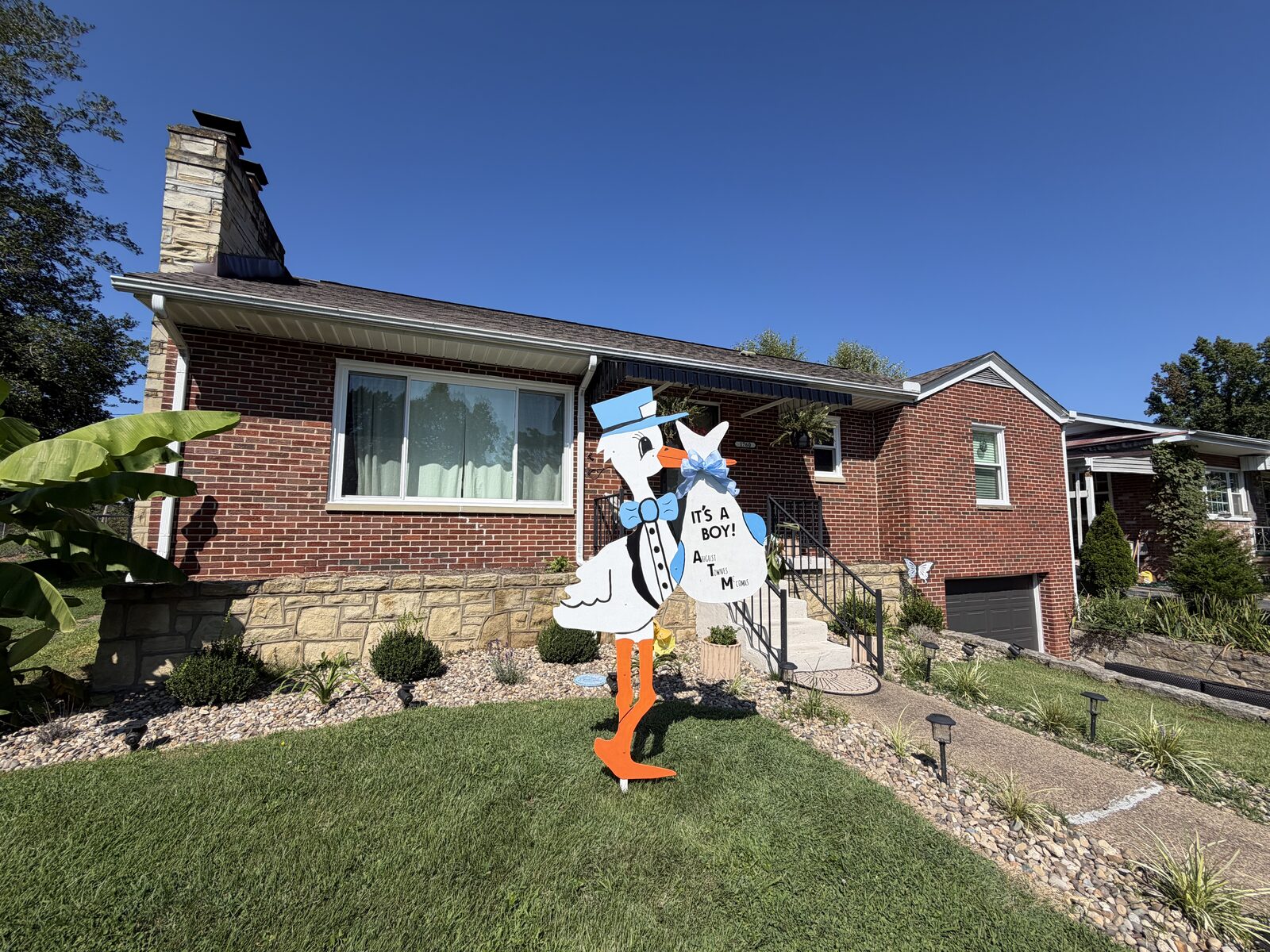 The blue stork sign viewed from the front walkway of a brick home.